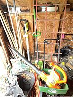 Wide view of shed corner showing leaf blower, spreader, power trimmers, extension cord and long-handled tools