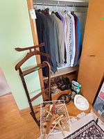 Closet view showing jackets, shirts, pants, shoes, hat, valet stand, basket of brushes