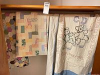 Three quilts hanging: hexagon patchwork, pastel block patchwork, embroidered teddy bear prayer