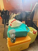 Overview of stacked camping items including cooler, lantern, water jugs and folded chairs