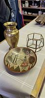 Group view of brass vase, folk art metal plate, and glass-brass terrarium