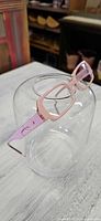 Full view of light pink Anne et Valentin eyeglass frames resting on clear glass surface