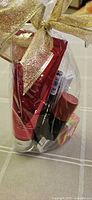 Clear cellophane-wrapped cosmetic gift set with gold ribbon showing various makeup items