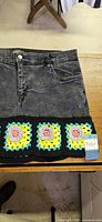Front view of black denim skirt with colorful crochet trim and attached Matico tag visible