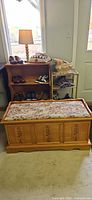 Front view of honey wood hope chest with floral cushion and painted panels