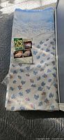 Folded twin bedspread with floral print, blue scalloped border, partial plastic sleeve and insert card visible