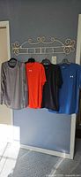 Four Under Armour performance shirts hanging, showing colors and sleeve lengths