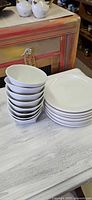 Stack of eight white porcelain cereal/soup bowls beside stack of eight white porcelain dinner plates
