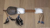 Front view showing dark turtle shell, fur cuffs, feathers and beads