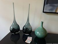 Two smoky grey blown glass vases and one turquoise pottery vase on tabletop