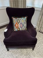 Front view of plum velvet wingback chair with decorative pillow