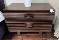 Front view of nightstand showing slatted drawer fronts, wave pulls, block legs, top surface