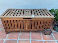 Full view of slatted wooden storage bench with wheels and lid closed