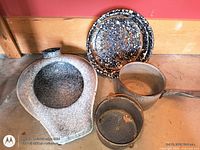 All four enamelware pieces laid out: bedpan, plate, saucepan, pot