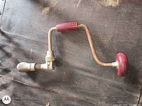 Overall view of metal brace drill showing red wooden handles and chuck