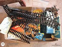 Top view showing train track pieces, play money, wooden tokens, dice and board-game boxes in cardboard box