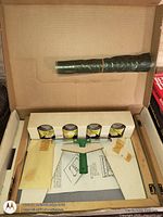 Open box showing ink cans, squeegee, rolled film, frame pieces, papers