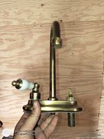 Full view of brass faucet showing spout, one ceramic lever handle and missing second handle