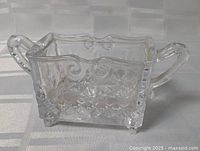 Front angle of clear pressed glass sugar bowl showing handles, patterns and feet