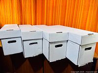 Four white long comic storage boxes closed, showing exterior condition