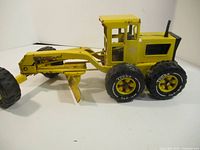 Left side view of yellow pressed-steel Tonka road grader showing wheels, cab and blade