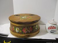 Front view of round tole painted wooden box with ceramic jar for scale
