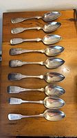 Top-down view of all ten sterling silver soup spoons arranged on wooden surface