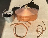 Entire moonshine still set laid out: copper boiler, galvanized bucket with coil, copper tubing sections