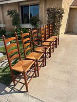 Six ladder-back chairs lined up outdoors