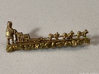 Front view of 10 kt gold dogsled brooch showing musher, sled, four dogs