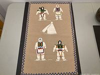 Full view of tapestry showing four beaded leather Inuit figures, central tent and blue stitched border