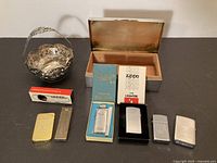Group shot of all lighters, flint dispenser, silverplate dish and cigarette box, lids open where applicable