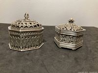 Front view of both sterling boxes closed showing pierced sides and finial tops