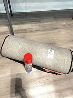 Rolled rug showing backing and tag with cleaner can beside
