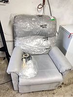 Front view of grey Pride lift chair still in plastic with remote and manual resting on seat