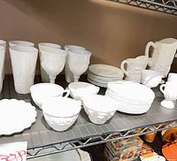 Shelf view of mixed milk glass tumblers, goblets, plates, teacups, pitcher