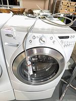 Front angled view of Whirlpool Duet Steam washer on pedestal with hoses draped