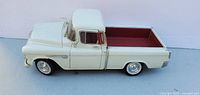 Side view of white 1955 Chevrolet die-cast pickup showing exterior and red bed