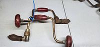 Two metal hand brace drills with red wooden handles