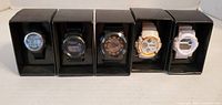 Front view of five boxed digital watches showing assorted colors and displays