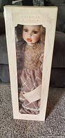 Front view of boxed porcelain doll showing dress and face