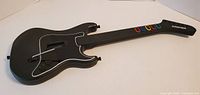 Front of black Les Paul style Guitar Hero controller showing fret buttons, strum bar, whammy bar
