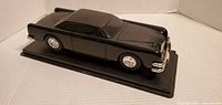 Left front three-quarter view of black diecast car on base