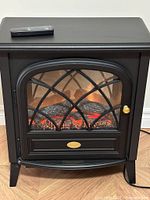 Front view of black electric fireplace heater with remote on top