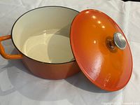 Dutch oven angled with lid partially open showing cream interior and orange exterior