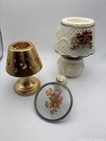 Three night-lights grouped: brass shade, ceramic rose lamp, floral round light