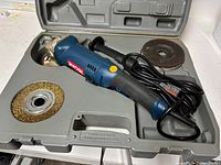 Open case showing angle grinder, wire cup wheel, grinding disc, and cord