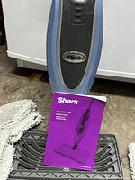 Front view of Shark steam mop body with manual, pad, and base tray visible