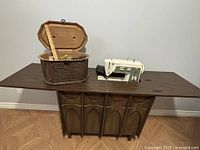 Cabinet fully opened with sewing machine and wicker basket on top