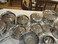 Overall view of stainless pots, pans, lids, steamer and bowls on table